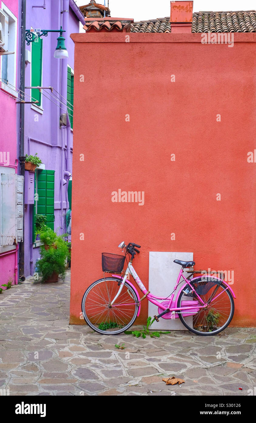 Pink bike appoggiato contro una parete colorata in un colorato street Foto Stock