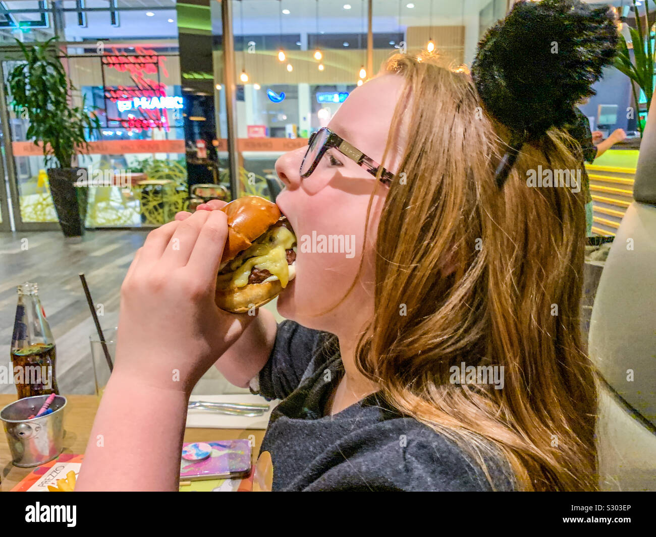 Ragazza giovane mangiare cheeseburger Foto Stock
