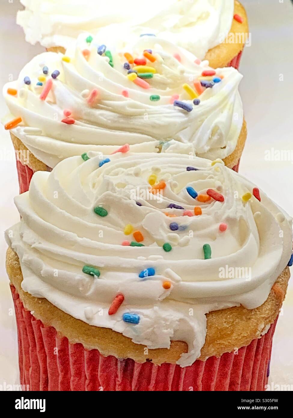 La vaniglia fresca tortine con glassa bianca e rainbow spruzza. Foto Stock