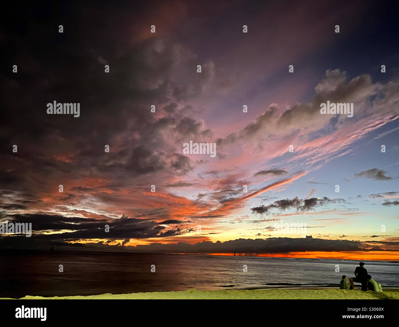 Tre persone che guardano un drammatico tramonto da una stretta striscia di spiaggia Foto Stock