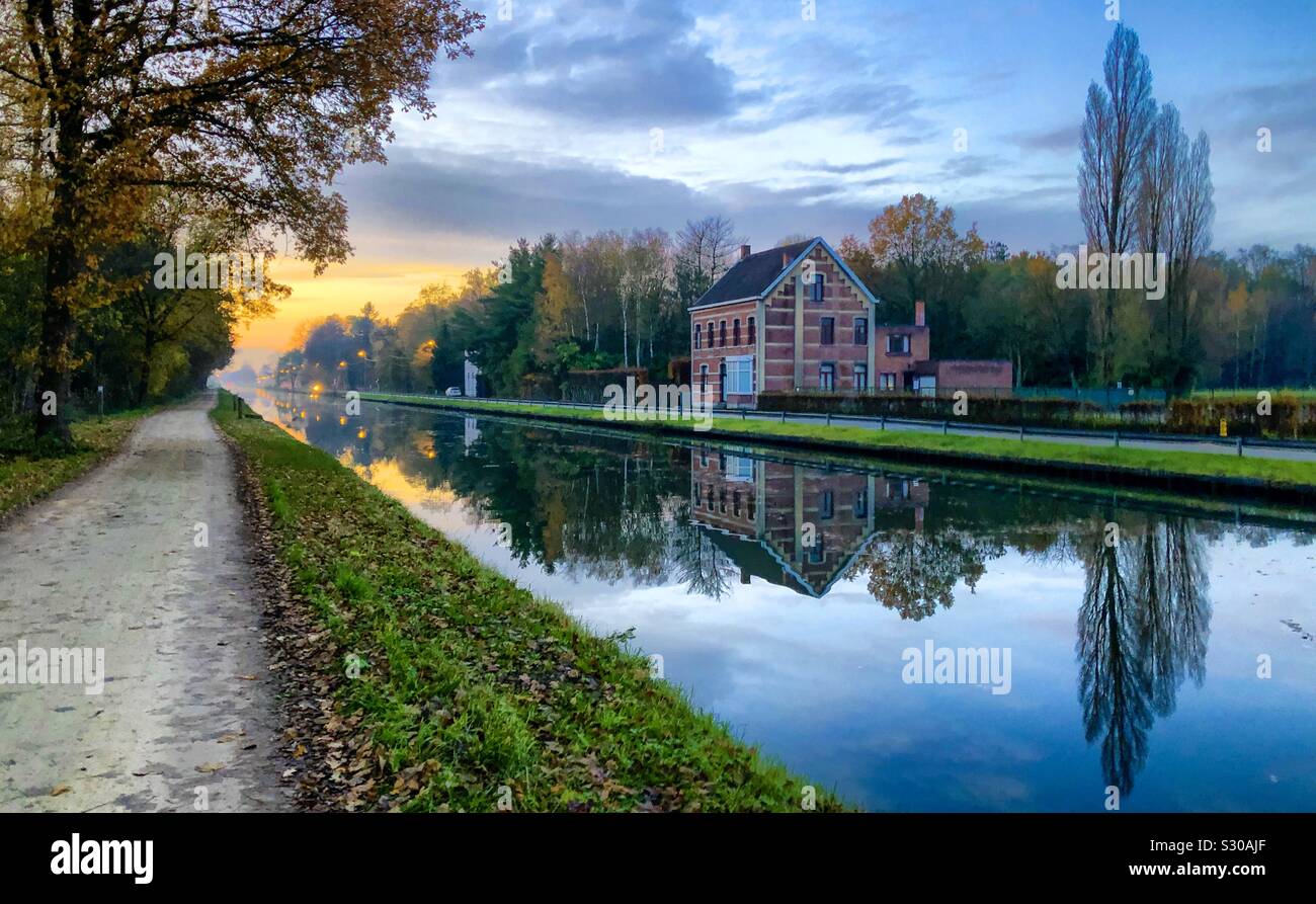 Accogliente casa riflessa nell'acqua del fiume o canale che fluisce attraverso una zona di foresta, tutto questo sotto un tramonto o l'alba sky - Immagine stock catturata con smartphone