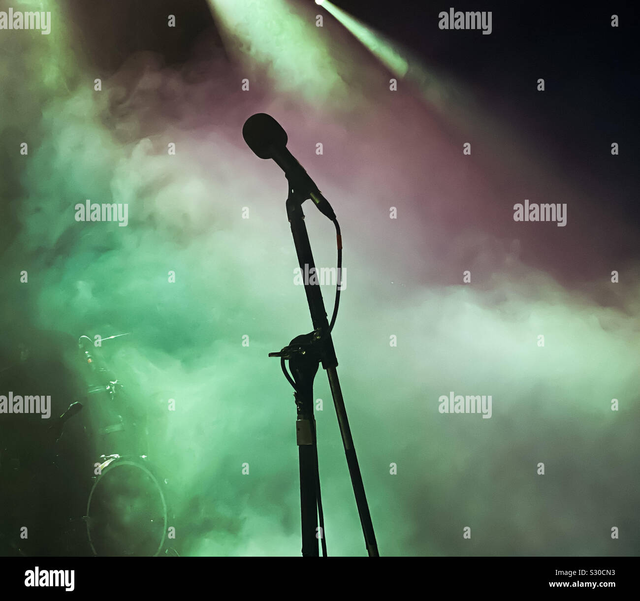 Microfono e stand stagliano su un palcoscenico di un concerto contro l'illuminazione e gli effetti del fumo - Immagine stock catturata con smartphone