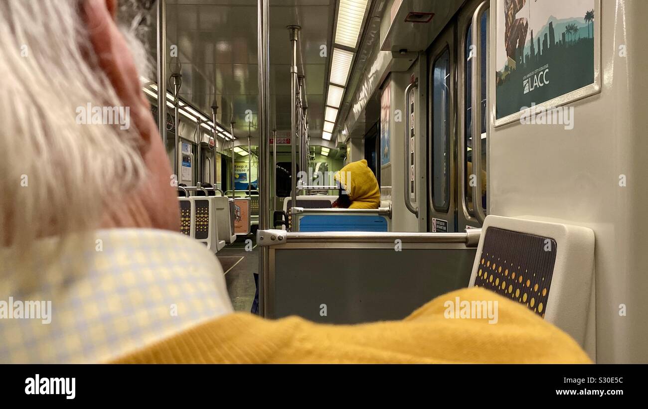 LOS ANGELES, CA, NOV 2019: vista sulla spalla dell'uomo in felpa gialla, guardando verso la persona in felpa con cappuccio giallo, equitazione la Metro linea viola treno della metropolitana Foto Stock