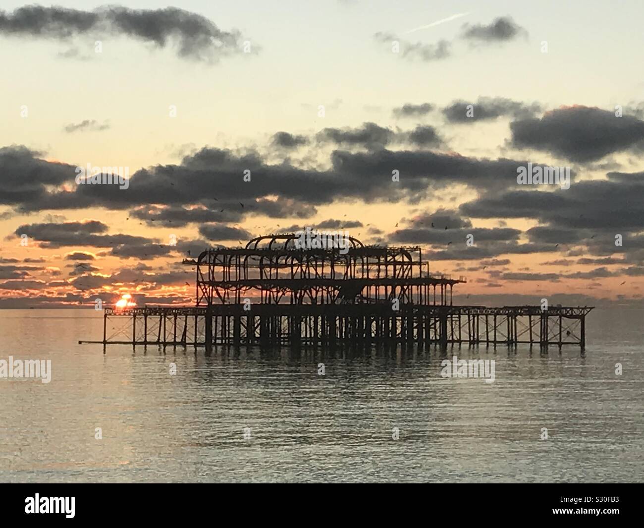 Tramonto dietro la bruciata Molo Ovest di Brighton. Foto Stock