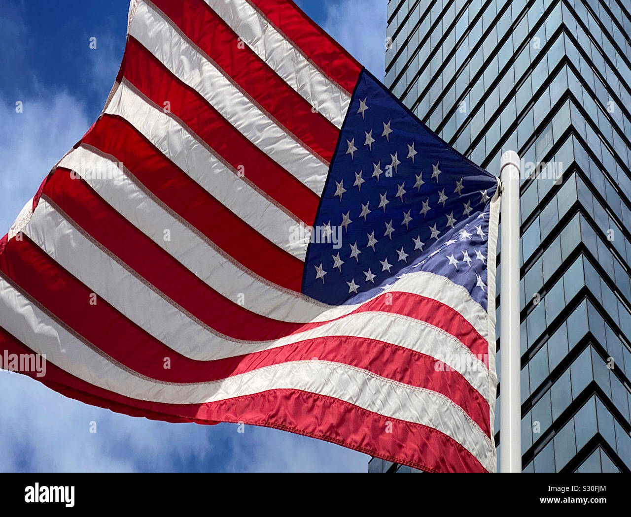 Bandiera americana battenti accanto a un moderno grattacielo di vetro Foto Stock