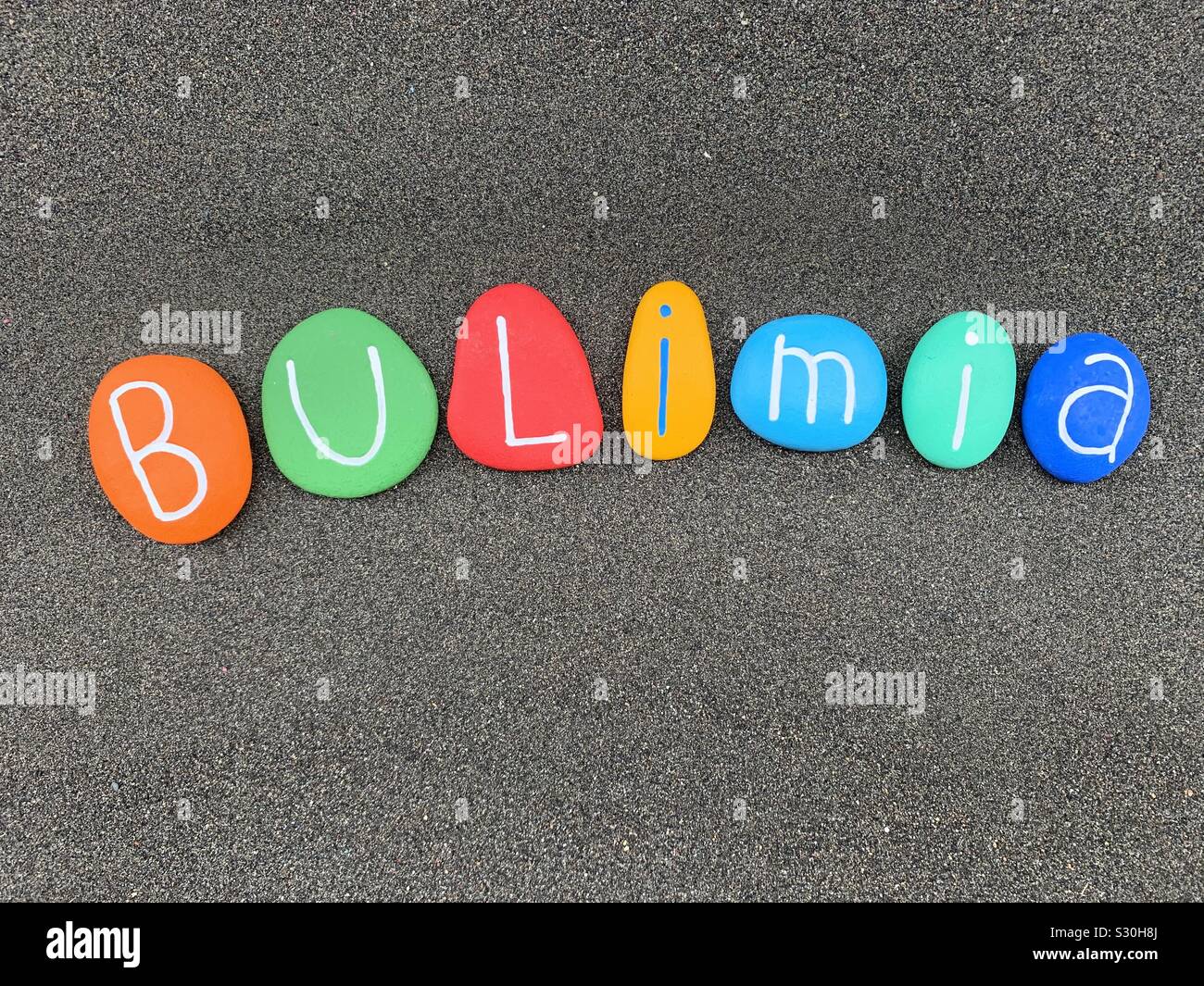 La bulimia nervosa, bulimia nervosa, gravi malattie mentali testo composto con multi Colored Stone lettere al di sopra di sabbia nera vulcanica Foto Stock