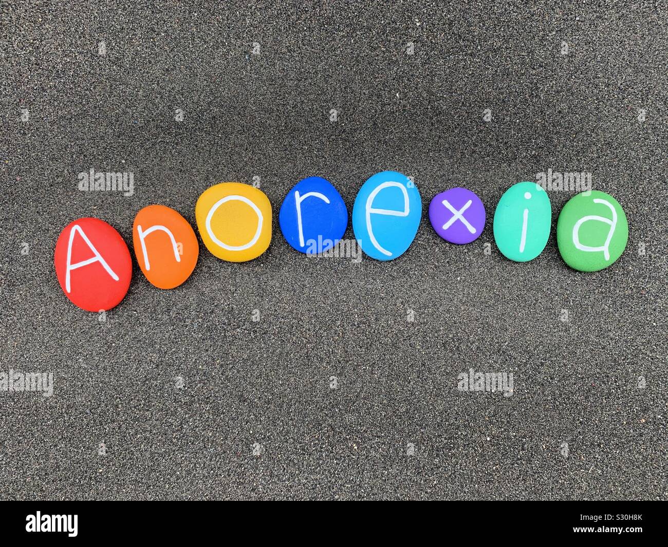 Anoressia, anoressia nervosa, disturbo alimentare malattia nome composto con multi Colored Stone lettere al di sopra di sabbia nera vulcanica Foto Stock