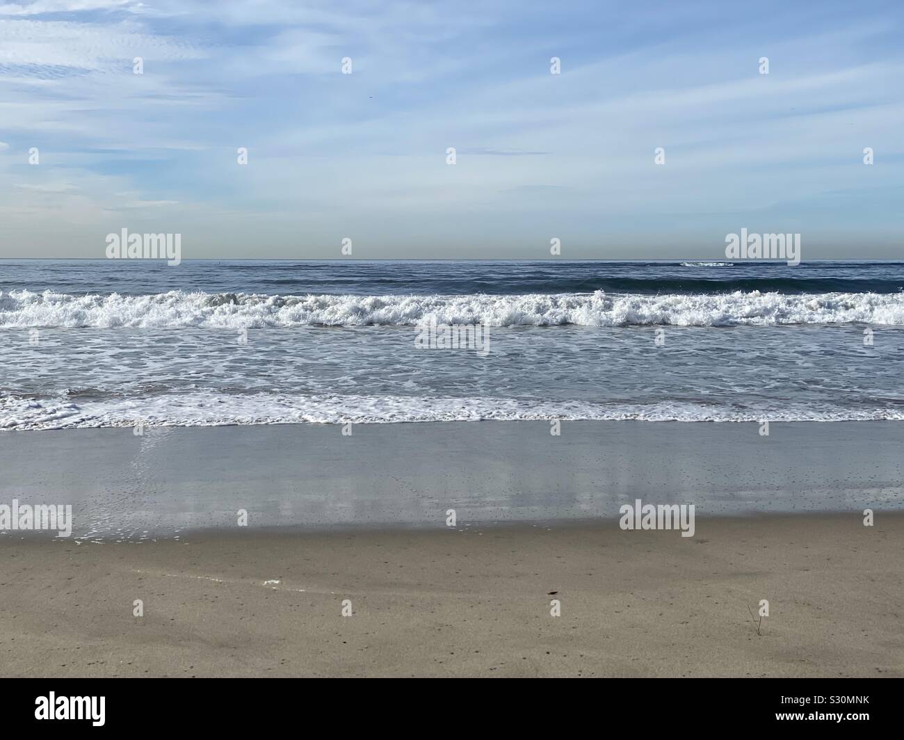 Pacific Ocean Waves a laminazione a riva sabbiosa con nebuloso cielo blu sopra Foto Stock