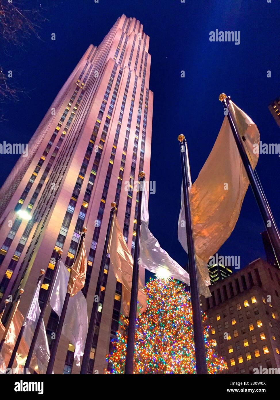 L'iconico albero di Natale brilla luminoso alla base del grattacielo roccia 30 ed è circondato da argento e oro bandiere durante la stagione delle vacanze, NYC, STATI UNITI D'AMERICA Foto Stock