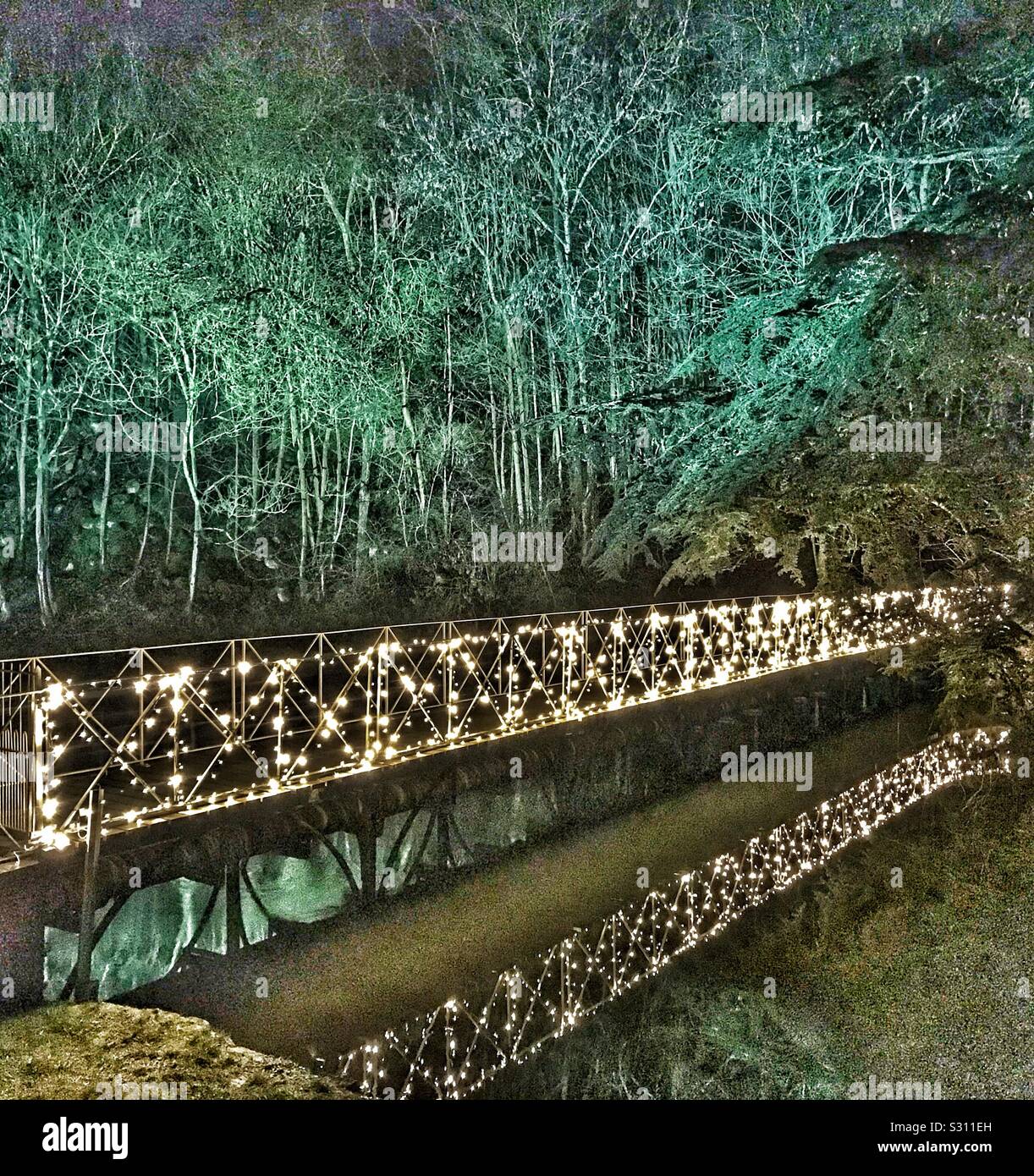 Il Palazzo di Blenheim e illuminata la luce di Natale Trail 2019. Ponte illuminato riflettente nel lago e gli alberi dietro con uplighting verde. Foto Stock