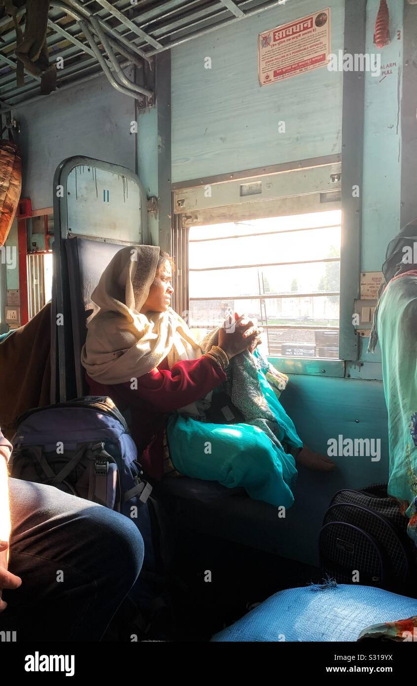 Una donna indiana seduta accanto a una finestra su un treno indiano in classe senza riserve Foto Stock