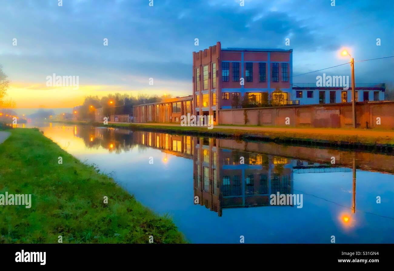 Antico edificio industriale riflesso in un canale all'alba, Kempen, Belgio - Immagine stock catturata con smartphone
