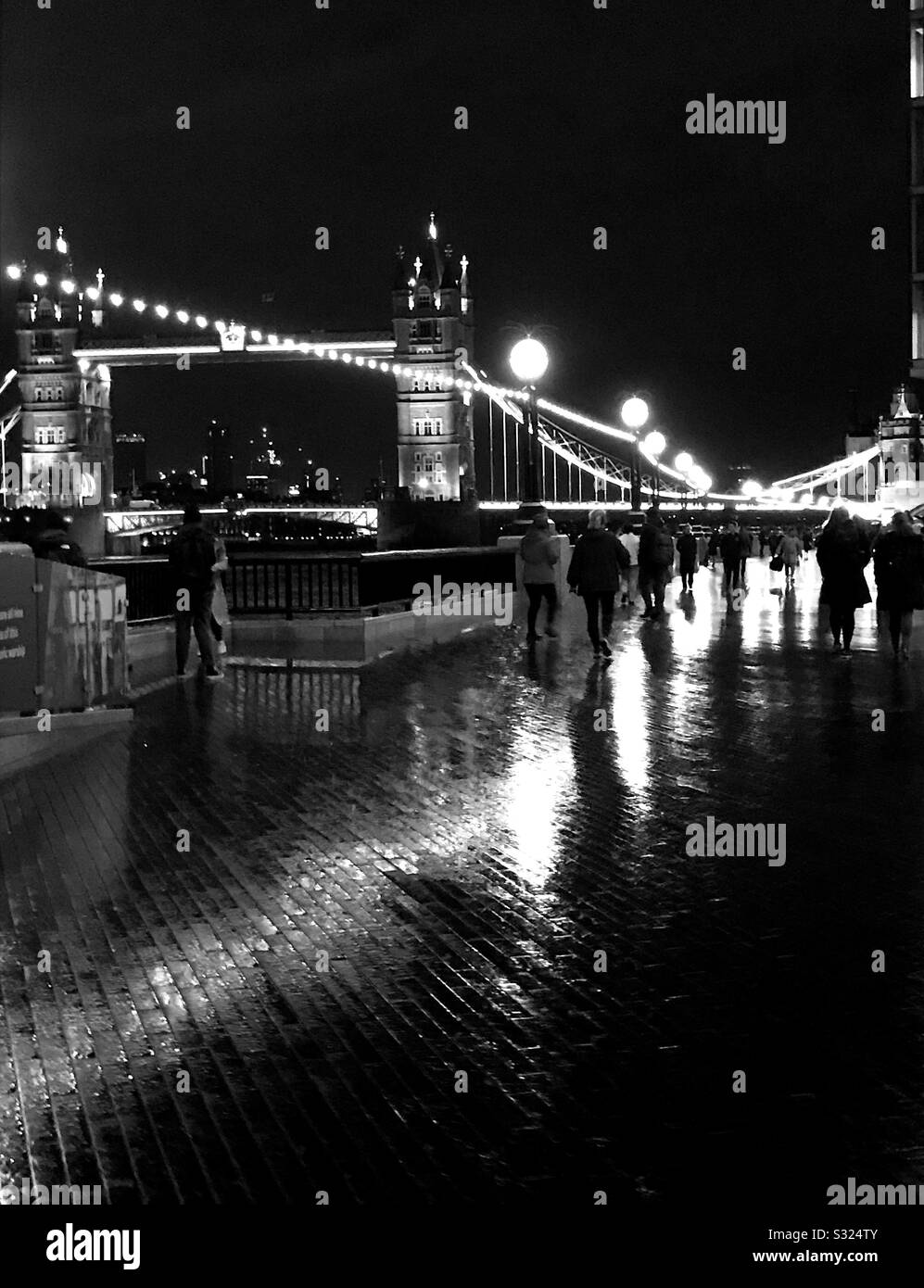 Figure che camminano lungo la riva sud del Tamigi di notte, con Tower Bridge sullo sfondo, bianco e nero Foto Stock