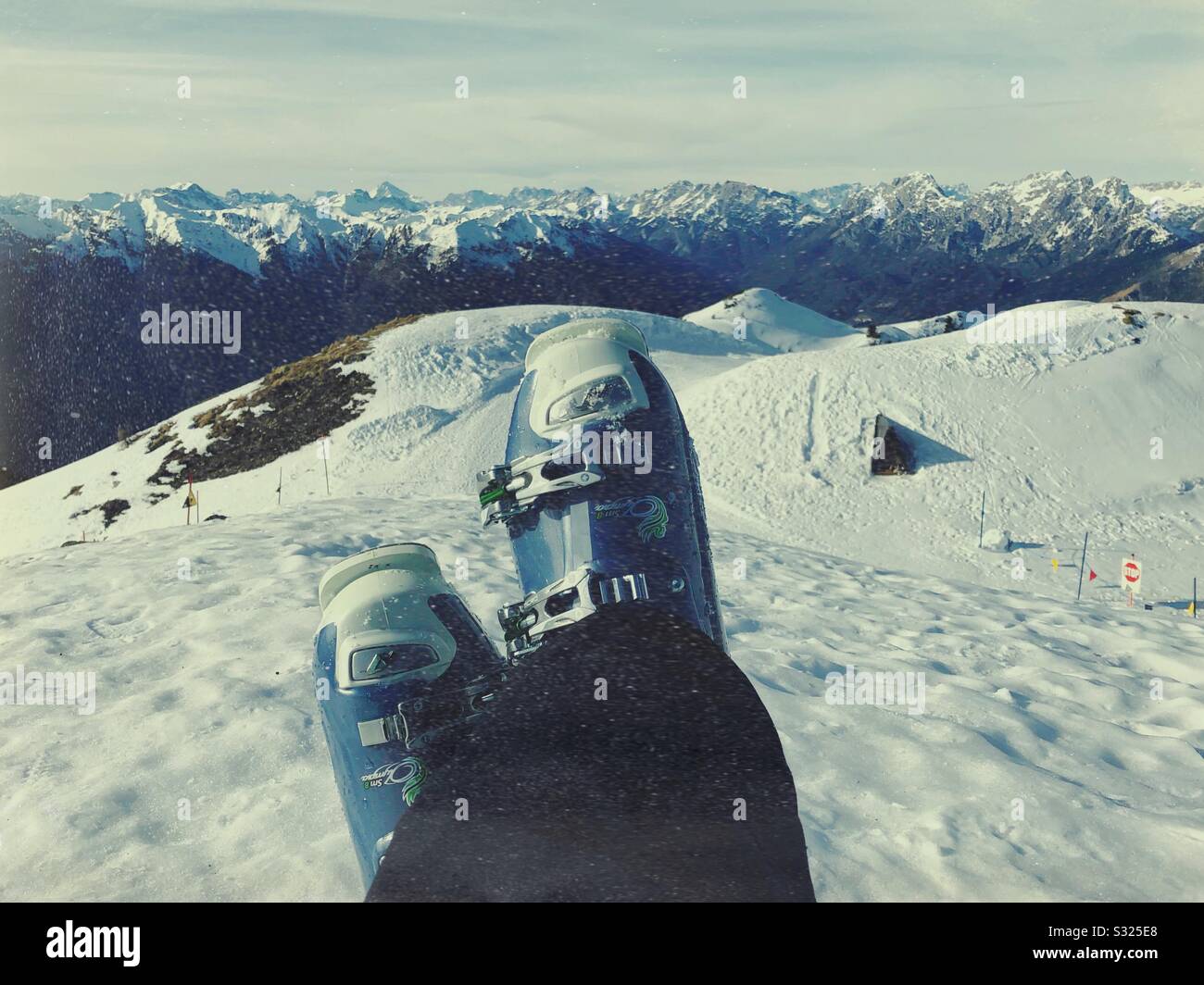 Gambe negli scarponi da sci che si trovano sulla neve in cima al comprensorio sciistico di Zoncolan, Italia. Dolomiti sullo sfondo. Foto Stock