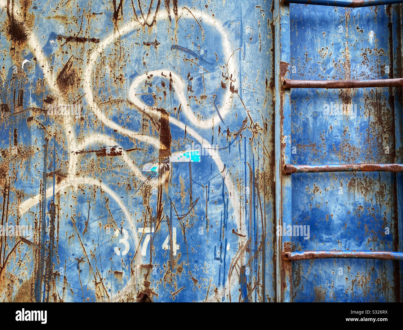 Lato di un cassonetto con segni di ruggine, graffiti e una scala Foto Stock