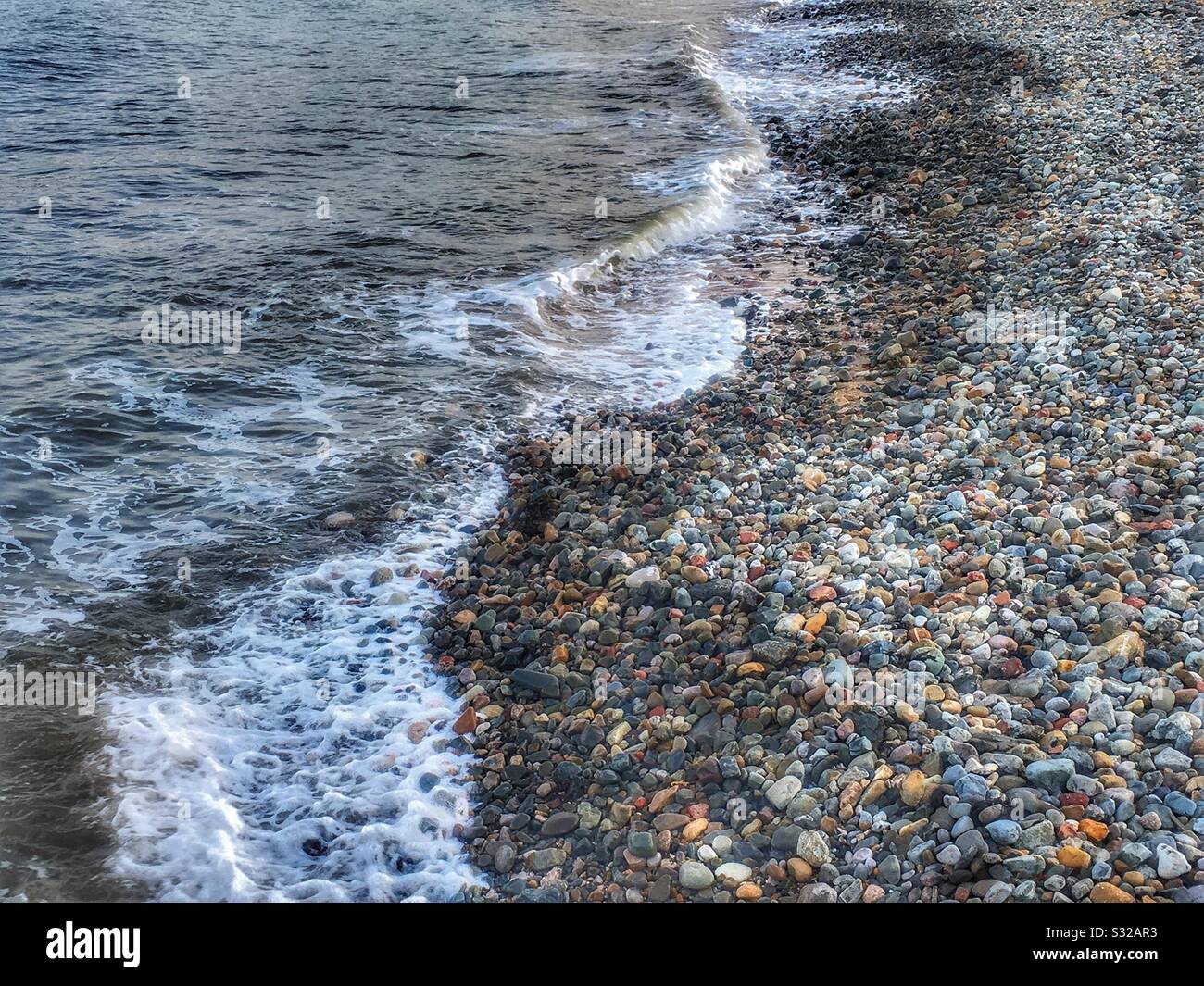 La marea che arriva su una spiaggia di ciottoli Foto Stock