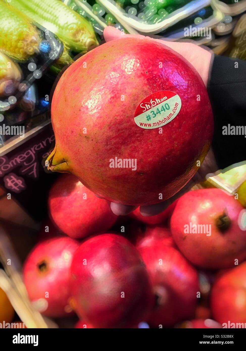 Melograni rosso brillante per la vendita nella corsia della drogheria di un deposito della drogheria tenuto da un acquirente, gli Stati Uniti - Immagine stock catturata con smartphone