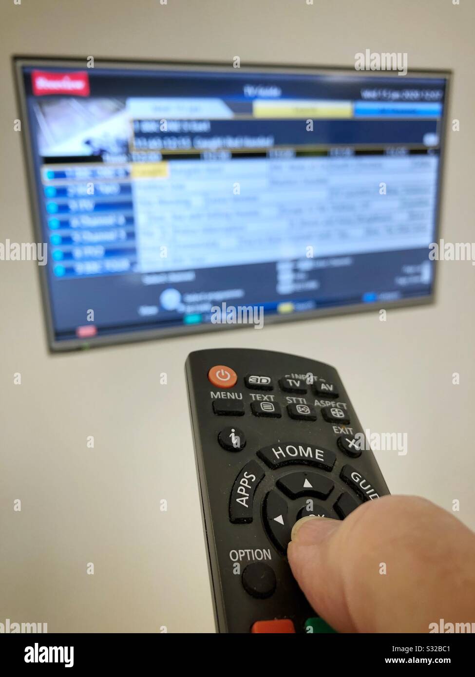 Tenere il telecomando con il pollice e premere il pulsante SELECT mentre si punta verso il televisore incorporato in una parete. - Immagine stock catturata con smartphone