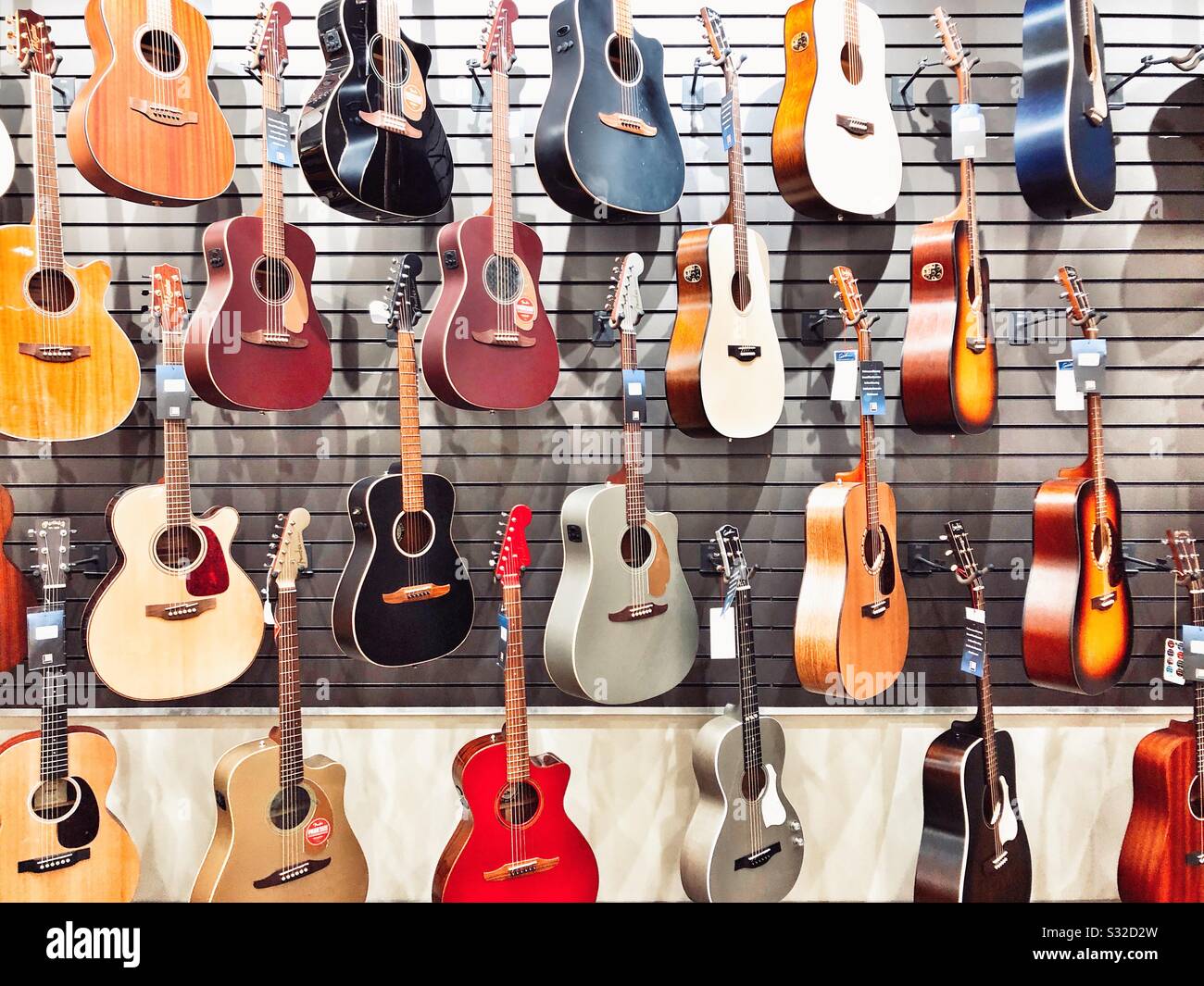Chitarre acustiche in una varietà di colori appesi a parete per la vendita in negozio di musica Foto Stock
