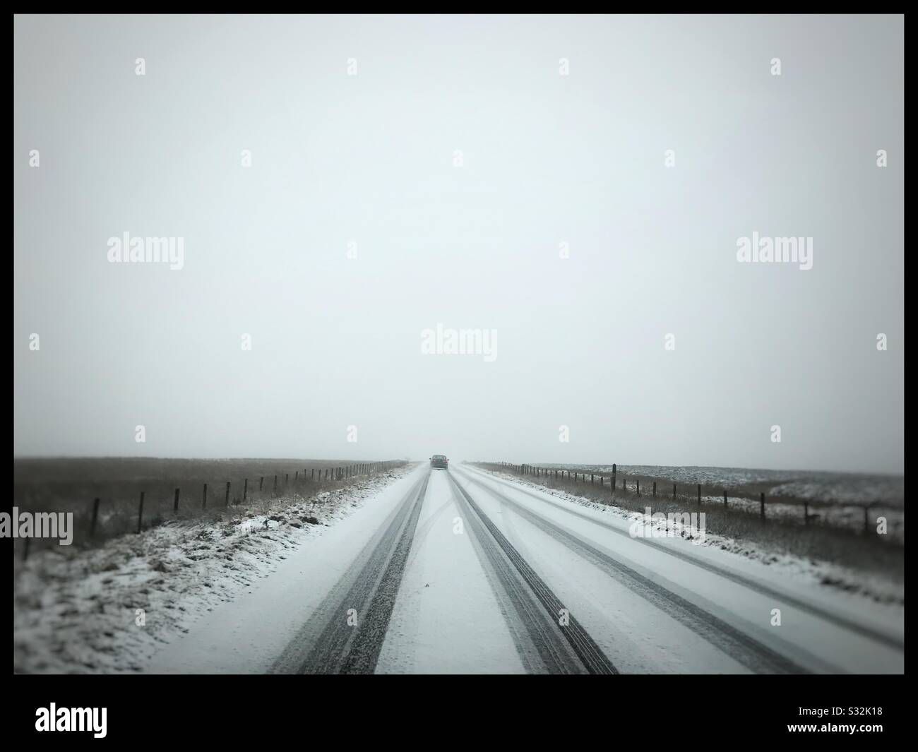 Una macchina lontana che guida nella neve su una strada attraverso le brughiere in inverno - Immagine stock catturata con smartphone