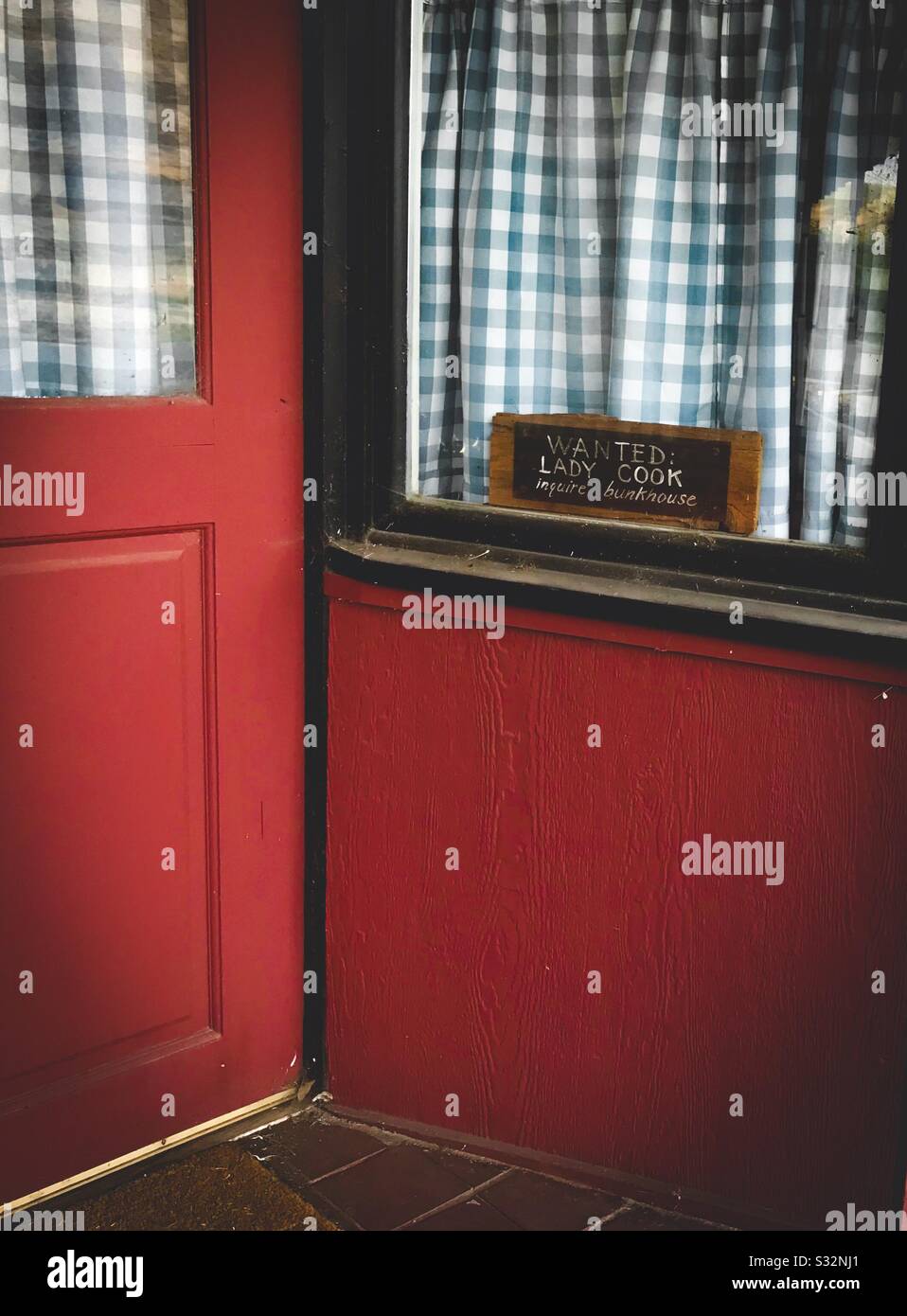 Finestra del ristorante con tende blu di gingham e un segno che dice "Wanted: Lady Cook Domandare Bunkhouse Foto Stock