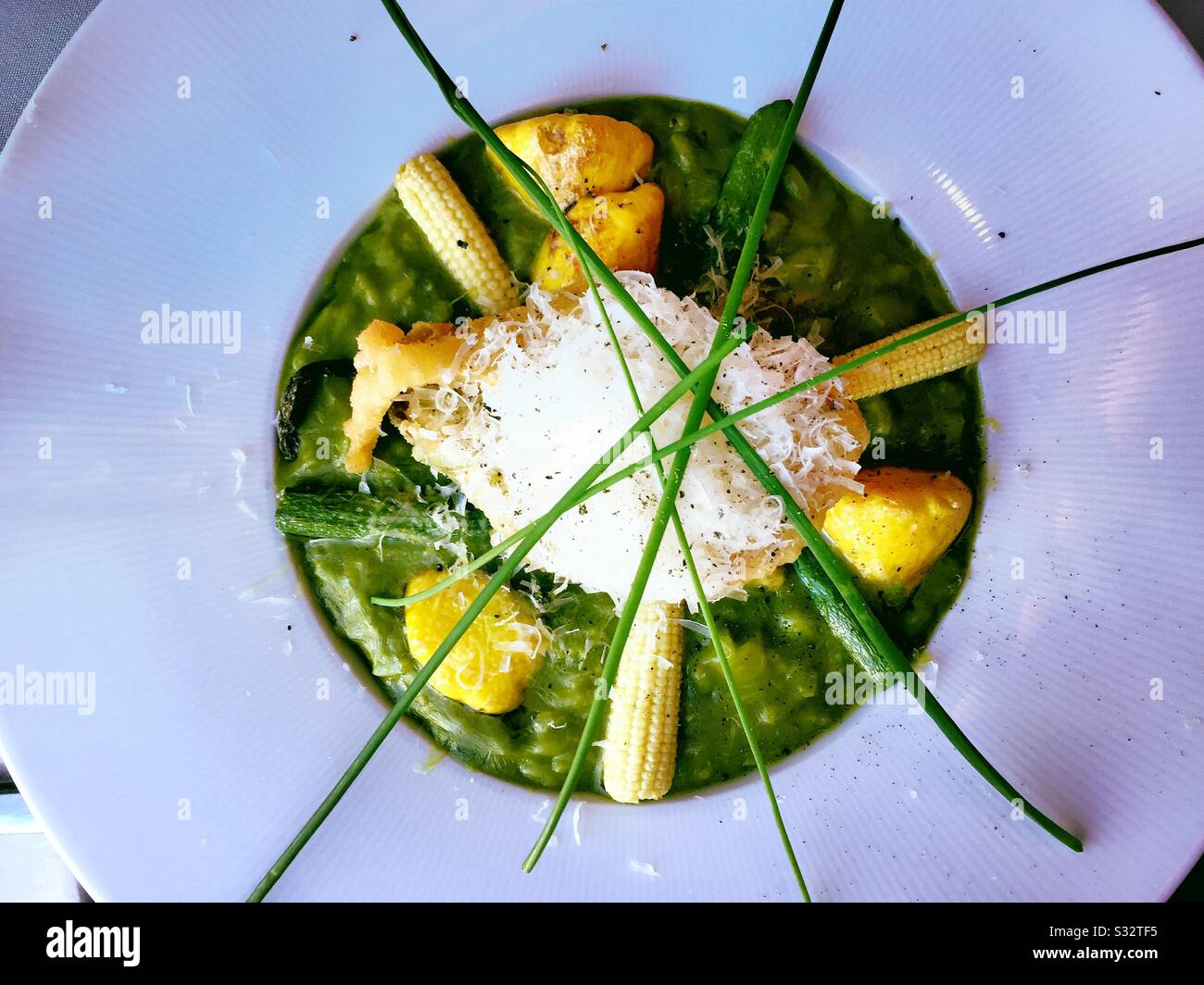 Piatto primo piano di un entrée gourmet di risotti di asparagi verdi serviti con mais, zucca patty pan e fiori di zucca, Stati Uniti - Immagine stock catturata con smartphone