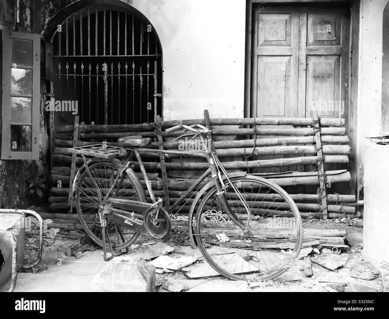 Un vecchio edificio che è usato per impilare cose una vecchia bicicletta, bastoni di bambù vecchia sedia di metallo, piastrelle di argilla spezzate con una finestra alla griglia e porta di legno, un classico aspetto vintage Foto Stock