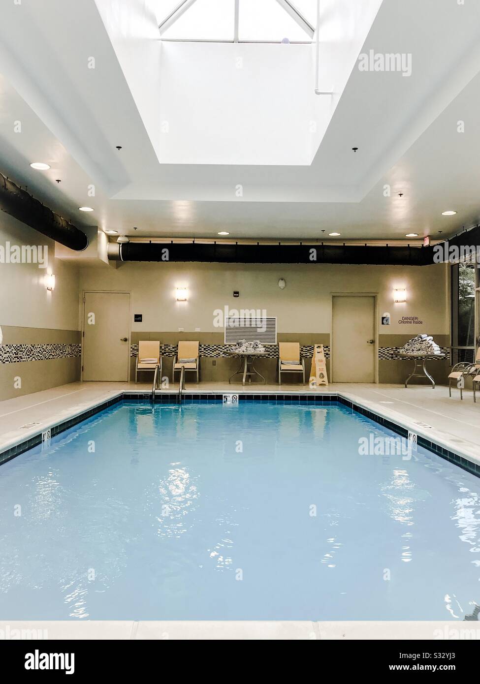 Piscina interna dell'hotel con illuminazione a soffitto e sedie gialle Foto Stock
