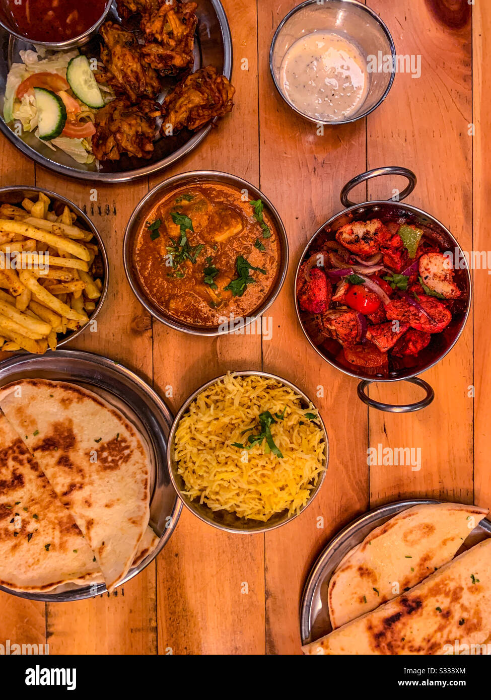 Selezione di cibo indiano ristorante in ciotole tra cui pollo tikka masala naan pane riso e patatine fritte Foto Stock