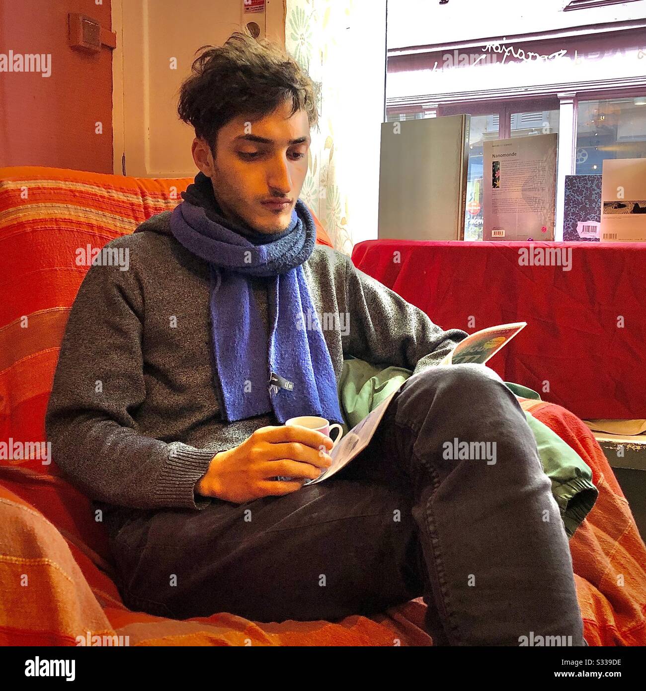 Giovane uomo che legge una rivista mentre si siede in una poltrona da caffè. Foto Stock