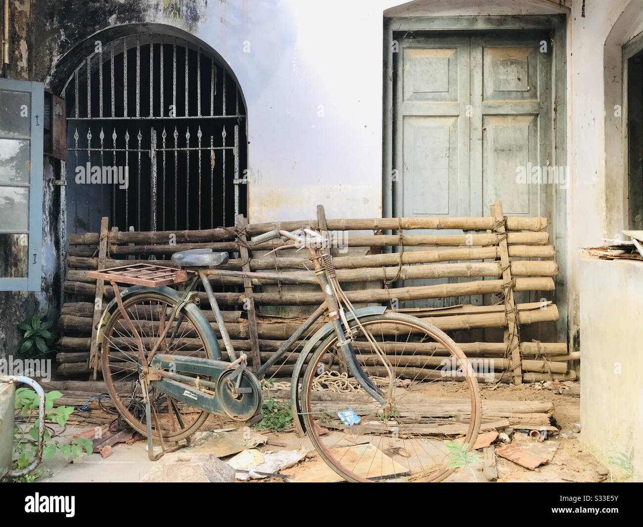Un vecchio edificio che è utilizzato per impilare le cose una vecchia bicicletta, bastoni di bambù vecchia sedia in metallo, piastrelle di argilla spezzata con una finestra alla griglia e porta in legno, un classico aspetto vintage - elementi rustici Foto Stock