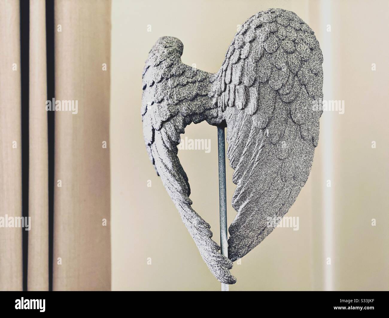 Un angelo ali ornamento statua, effetto pietra. Contro pareti pulite color crema e tende beige con spazio per le copie - Immagine stock catturata con smartphone