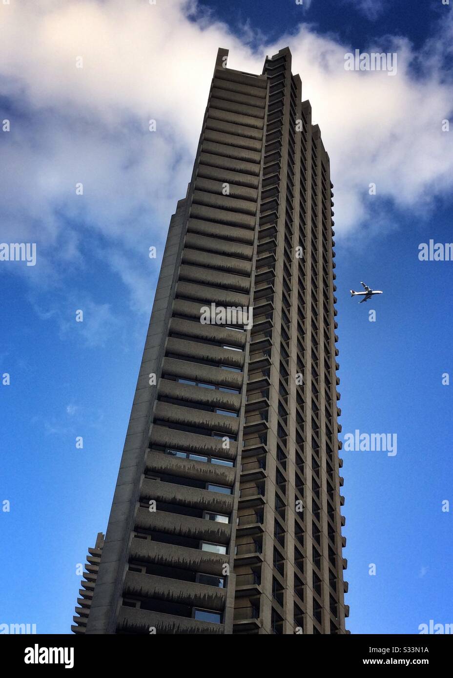 Un aereo vola oltre un blocco torre al Barbican a Londra, Regno Unito - Immagine stock catturata con smartphone