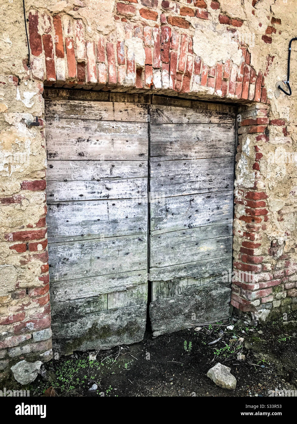 Porte a due fienile in legno grigio molto vecchio e sbiadito circondate da mattoni rossi e stucco beige in cemento. Foto Stock