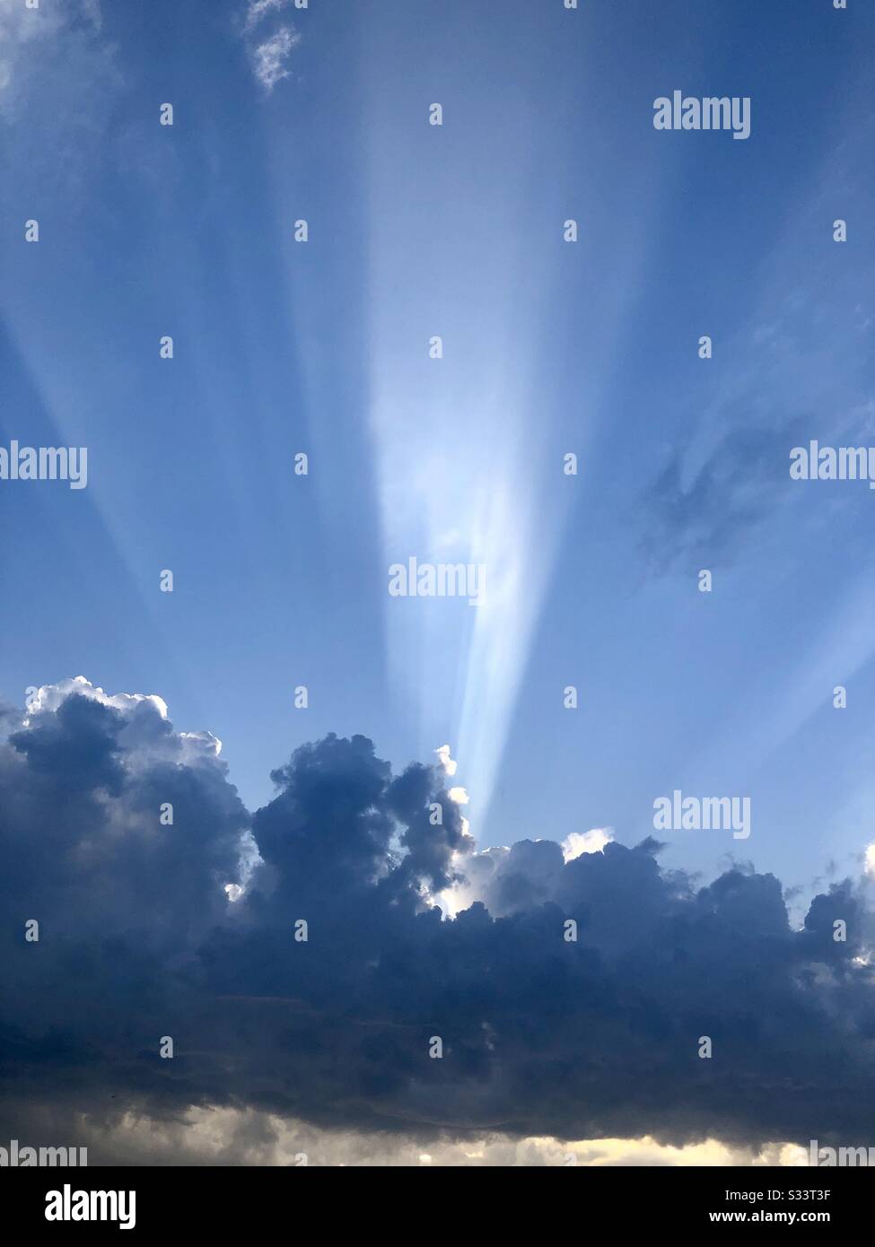 Un raggio di luce solare scoppia attraverso alcune nuvole scure che si profilano al tramonto Foto Stock