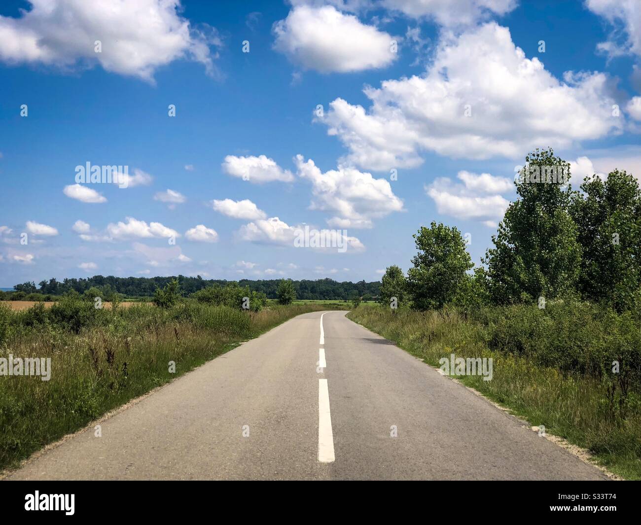 Strada vuota in una giornata di sole con nuvole bianche e soffici Foto Stock