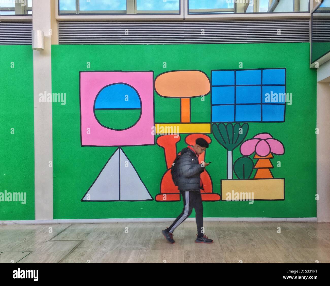 Ragazzo su smartphone a piedi di fronte a un colorato murale, Milton Keynes, Regno Unito - Immagine stock catturata con smartphone