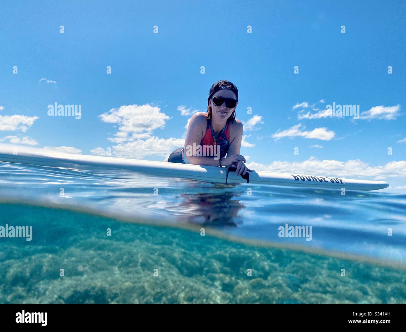Sopra-sotto di una femmina che posa su una tavola di racchetta di stanndup nell'oceano. Tavarua, Figi. Foto Stock