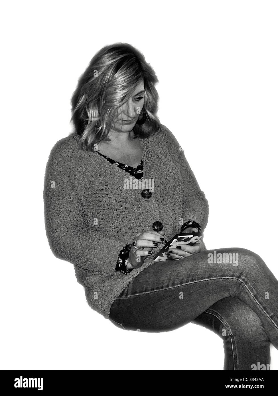 Donna isolata con capelli biondi senza sfondo seduta e utilizzando il suo telefono cellulare. Foto Stock