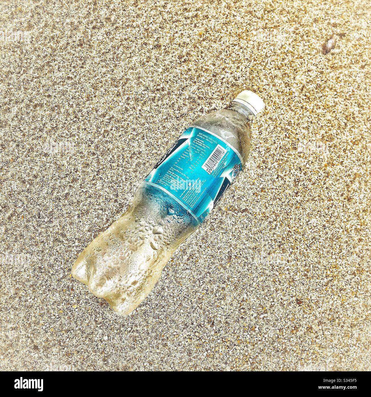 Bottiglia d'acqua in plastica parzialmente sepolta sulla spiaggia di Batu Rakit, Terengganu, Malesia - Immagine stock catturata con smartphone