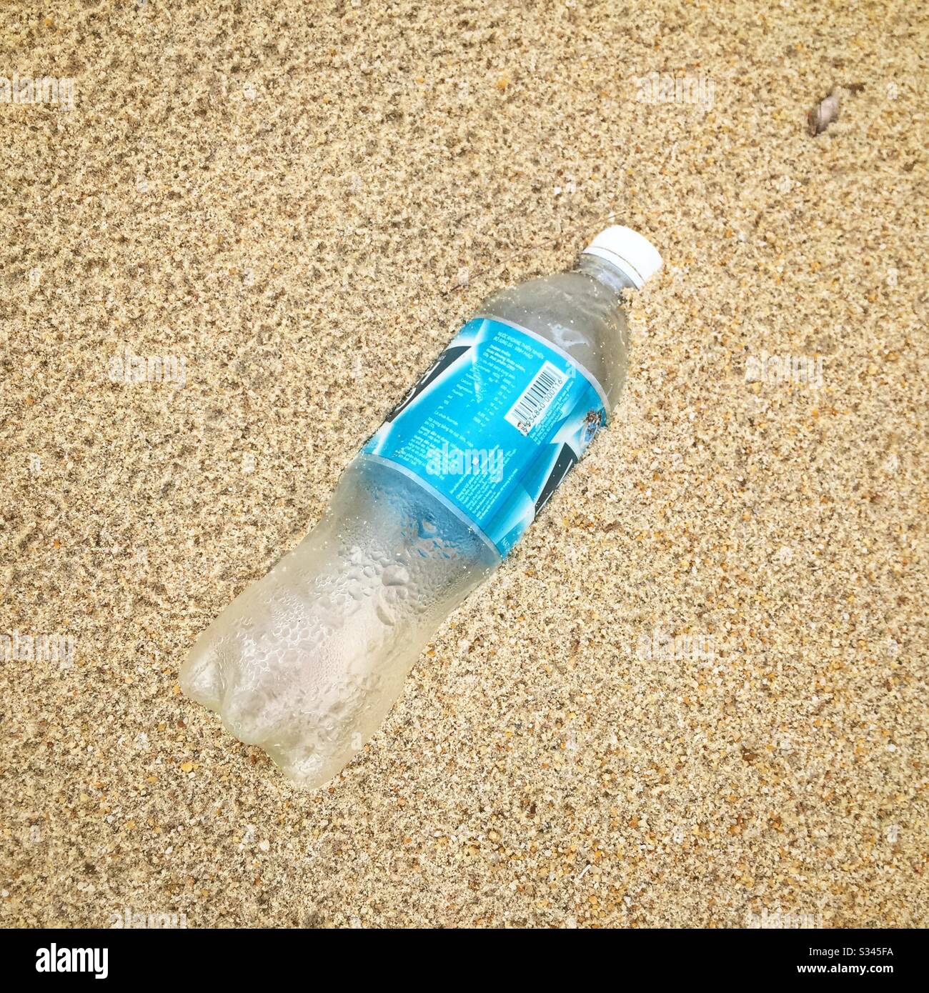Bottiglia d'acqua in plastica parzialmente sepolta sulla spiaggia di Batu Rakit, Terengganu, Malesia - Immagine stock catturata con smartphone