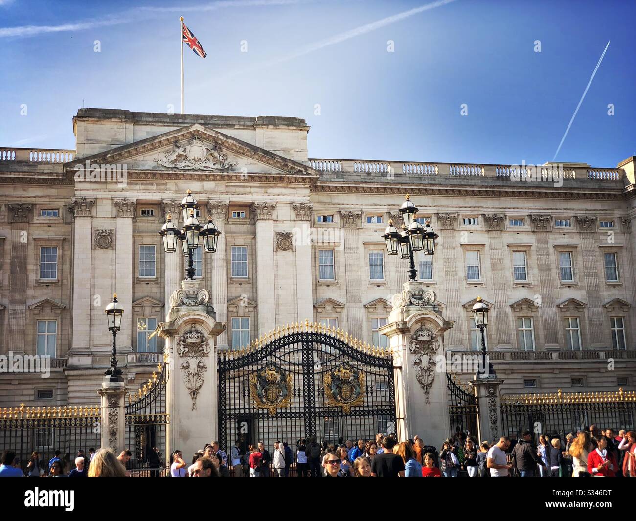 Una folla di turisti è vista alle porte di Buckingham Palace mentre l'Union Jack vola a pieno palo sotto un cielo blu a Londra, Regno Unito - Immagine stock catturata con smartphone