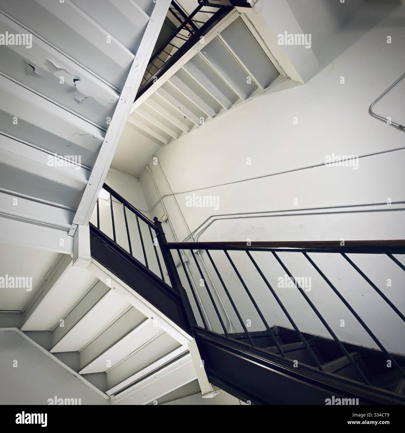 La scala interna forma un disegno astratto, simile all'arte di M C Escher, con un angolo inusuale dal basso. Composizione quadrata - Immagine stock catturata con smartphone