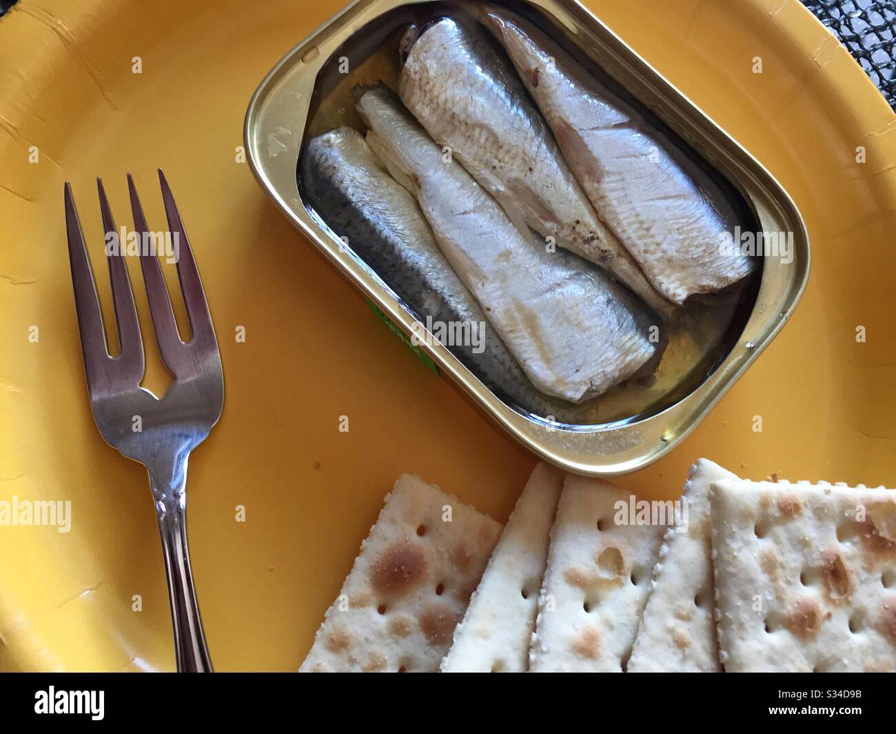 Piatto di una latta di sardine e cracker di saline con una forchetta su un piatto di carta giallo Foto Stock