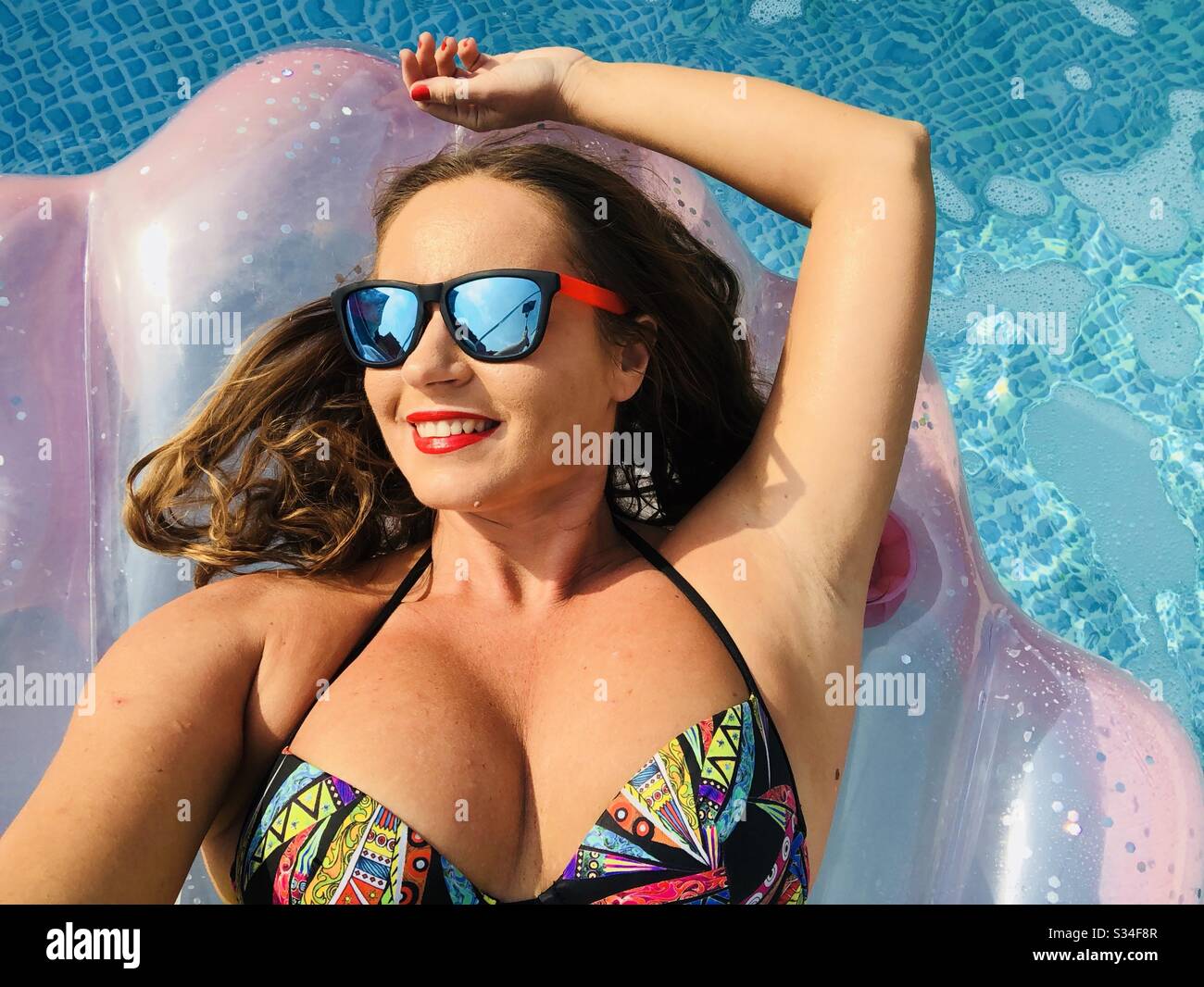 Donna che indossa occhiali da sole su un materasso gonfiabile piscina Foto Stock