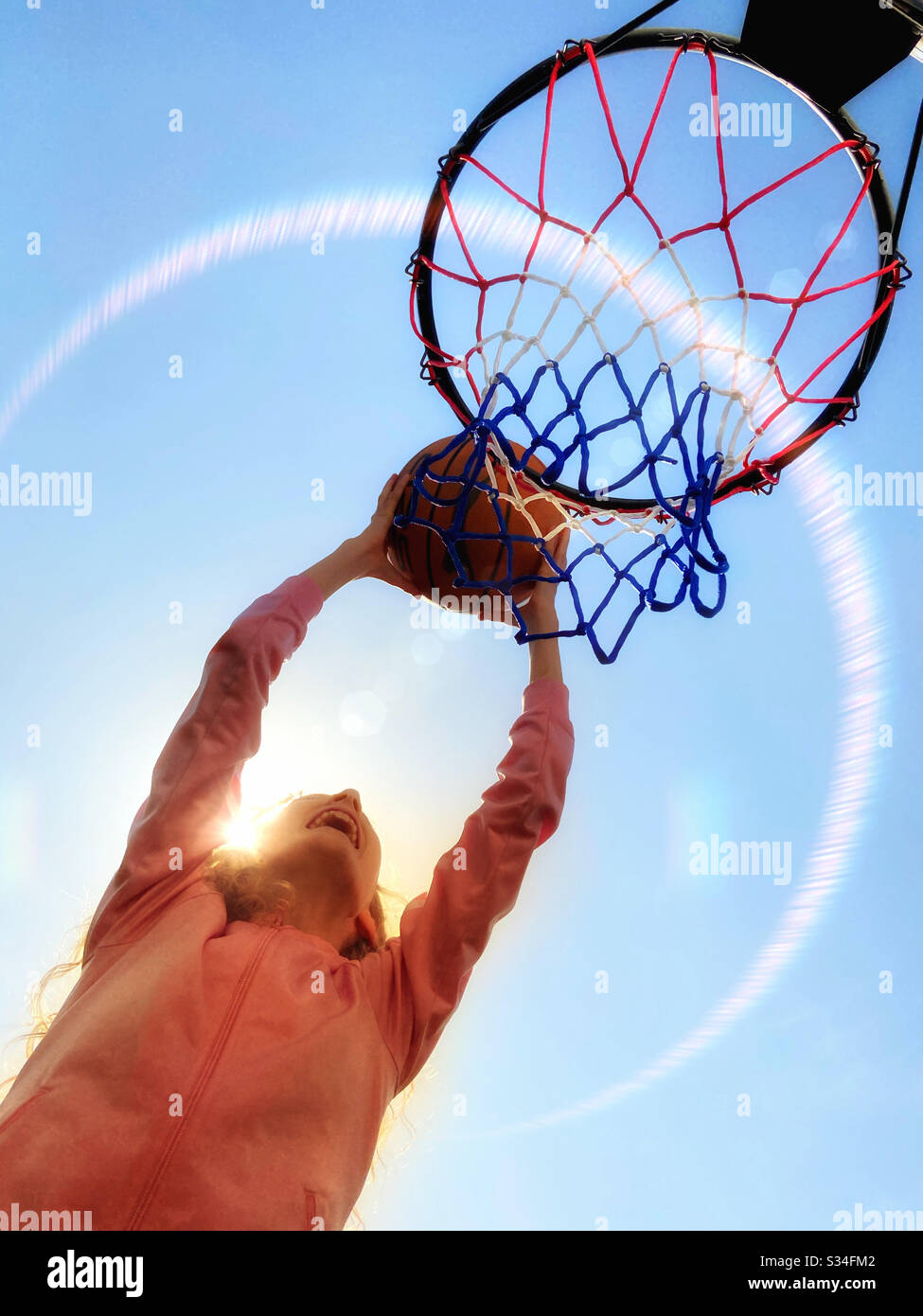 Giovane ragazza che ha incaparso pallacanestro in cerchio, retroilluminato dal sole. Foto Stock