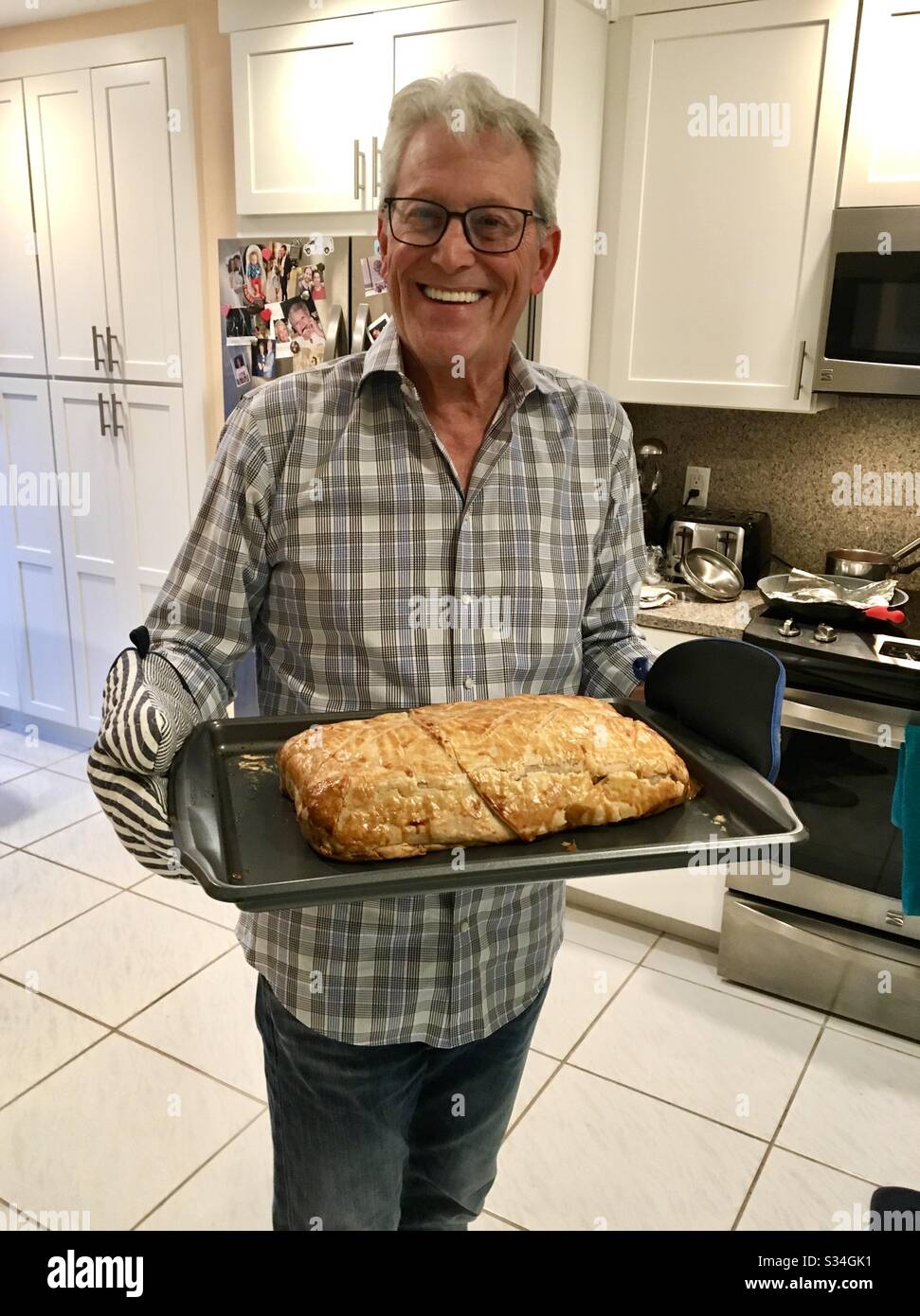 Uomo a casa che tiene la sua ricetta finita di salmone farcito con granchio avvolto in pasta sfoglia fresco dal forno. Foto Stock
