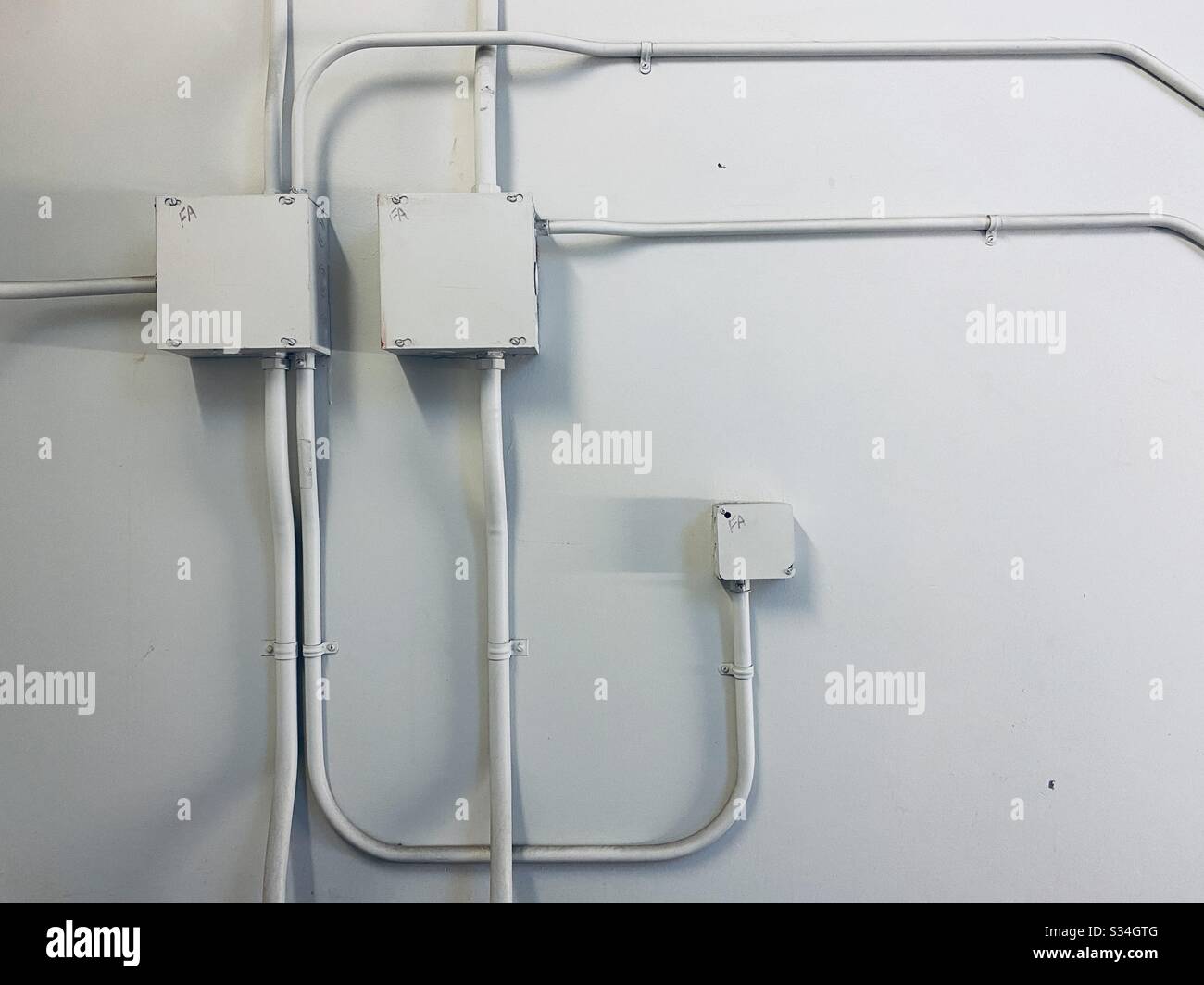 Parete bianca con condotti elettrici e scatole di giunzione che creano un modello astratto - Immagine stock catturata con smartphone