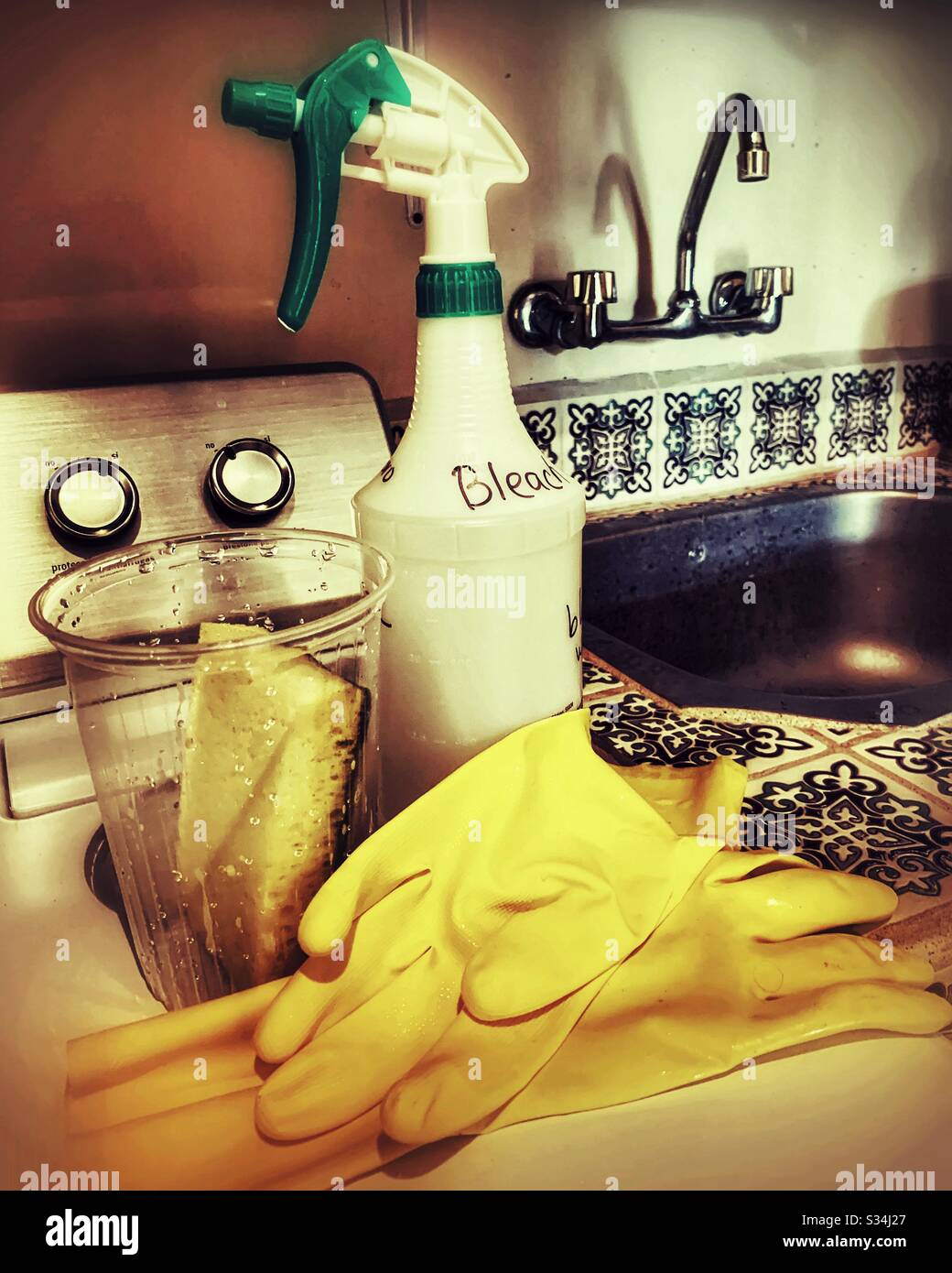 Una bottiglia spray con candeggina, un paio di guanti in gomma e una spugna fanno parte degli strumenti di disinfezione presenti in questa lavanderia. Foto Stock