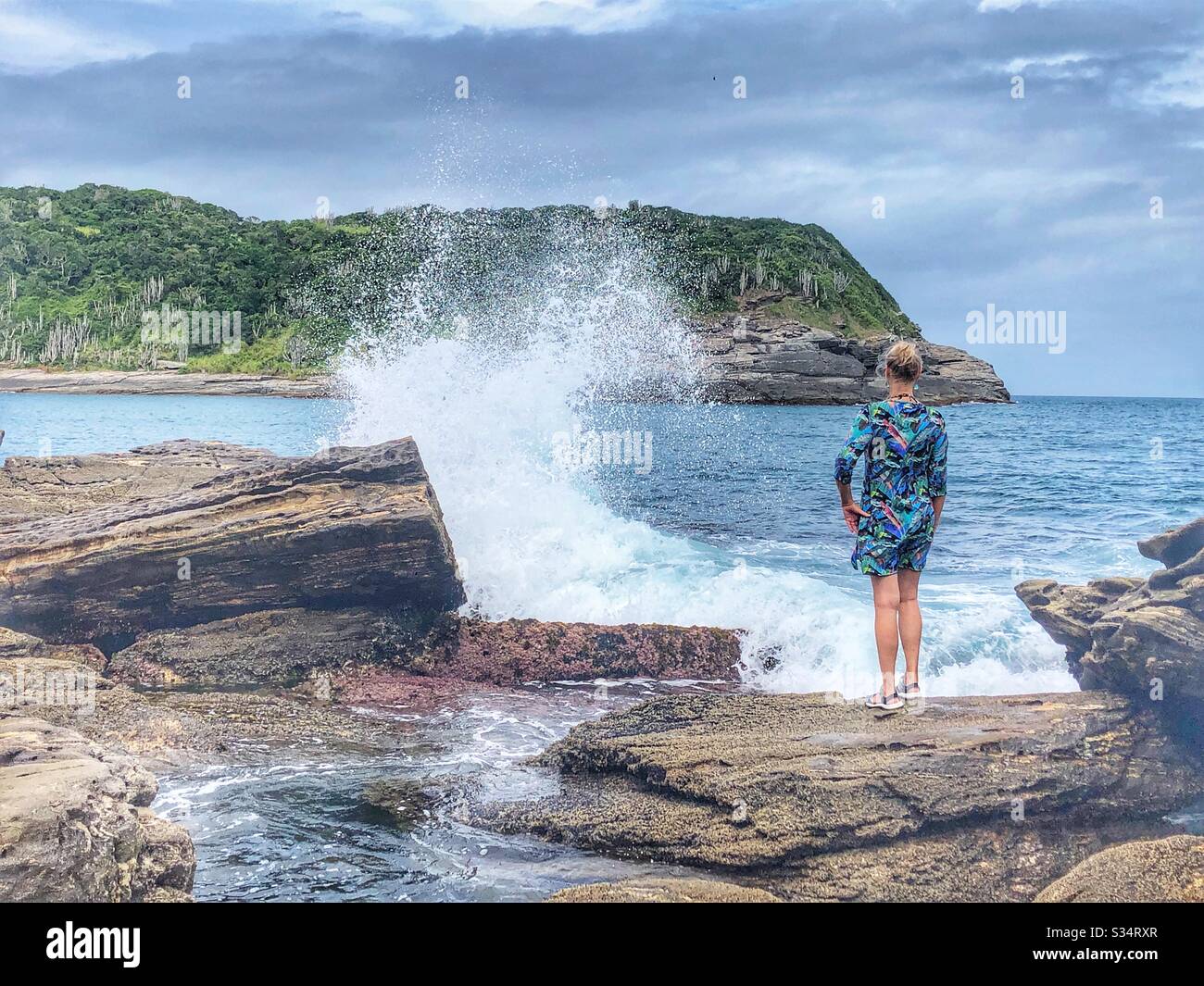 Una donna in piedi su una roccia che guarda verso il mare. Foto Stock